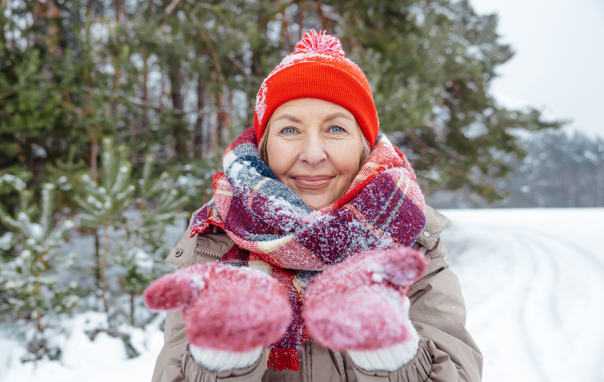 Kvinne i vintervær med lue og røde votter ser mot kamera.