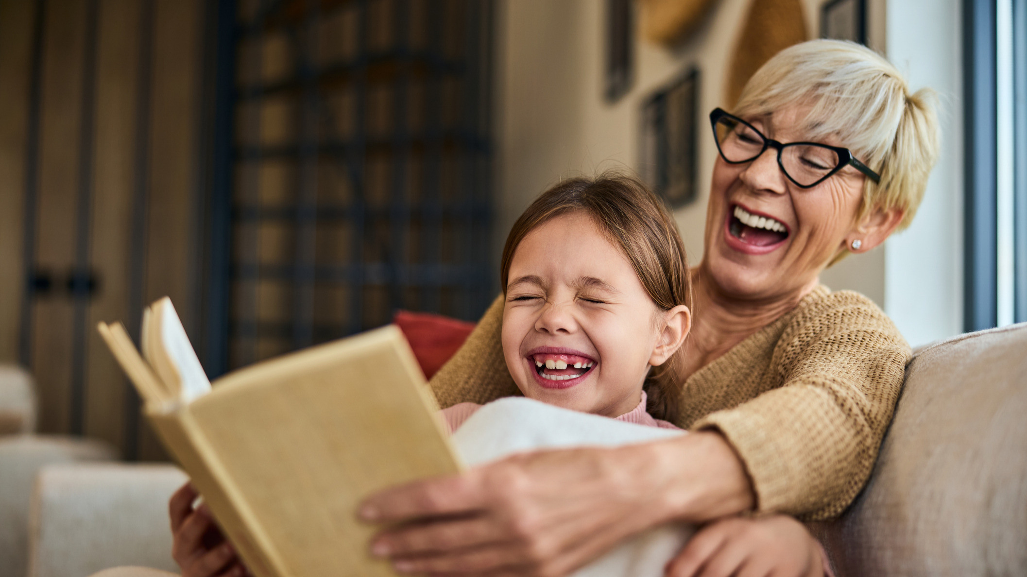 Bestemor og barnebarn leser bok og ler sammen