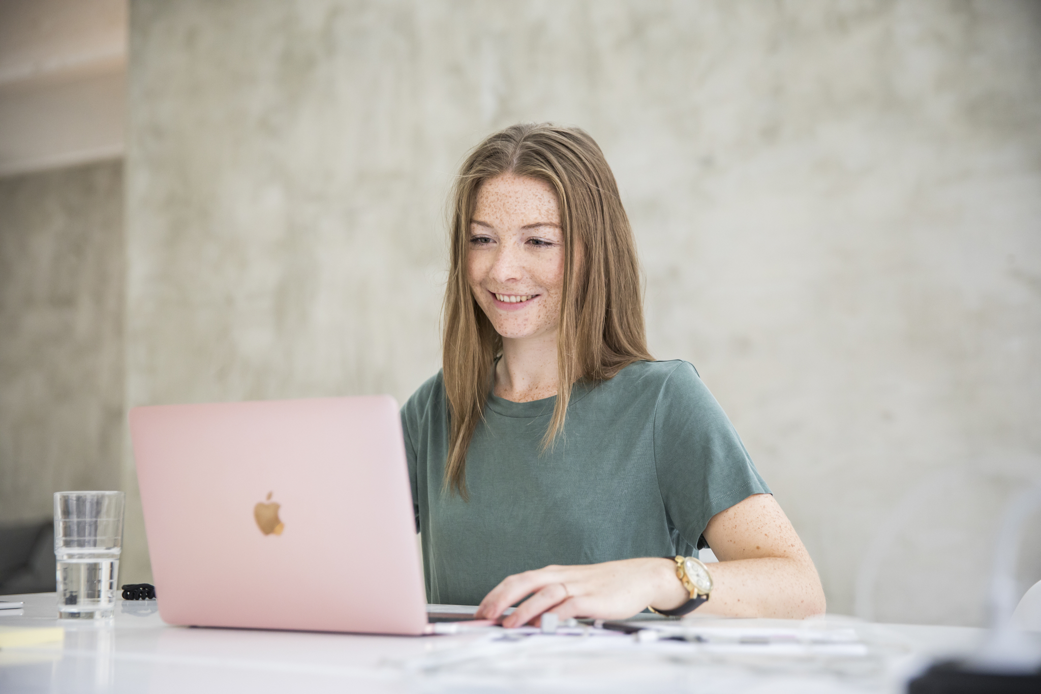 Ung kvinne sitter foran en Mac og jobber.