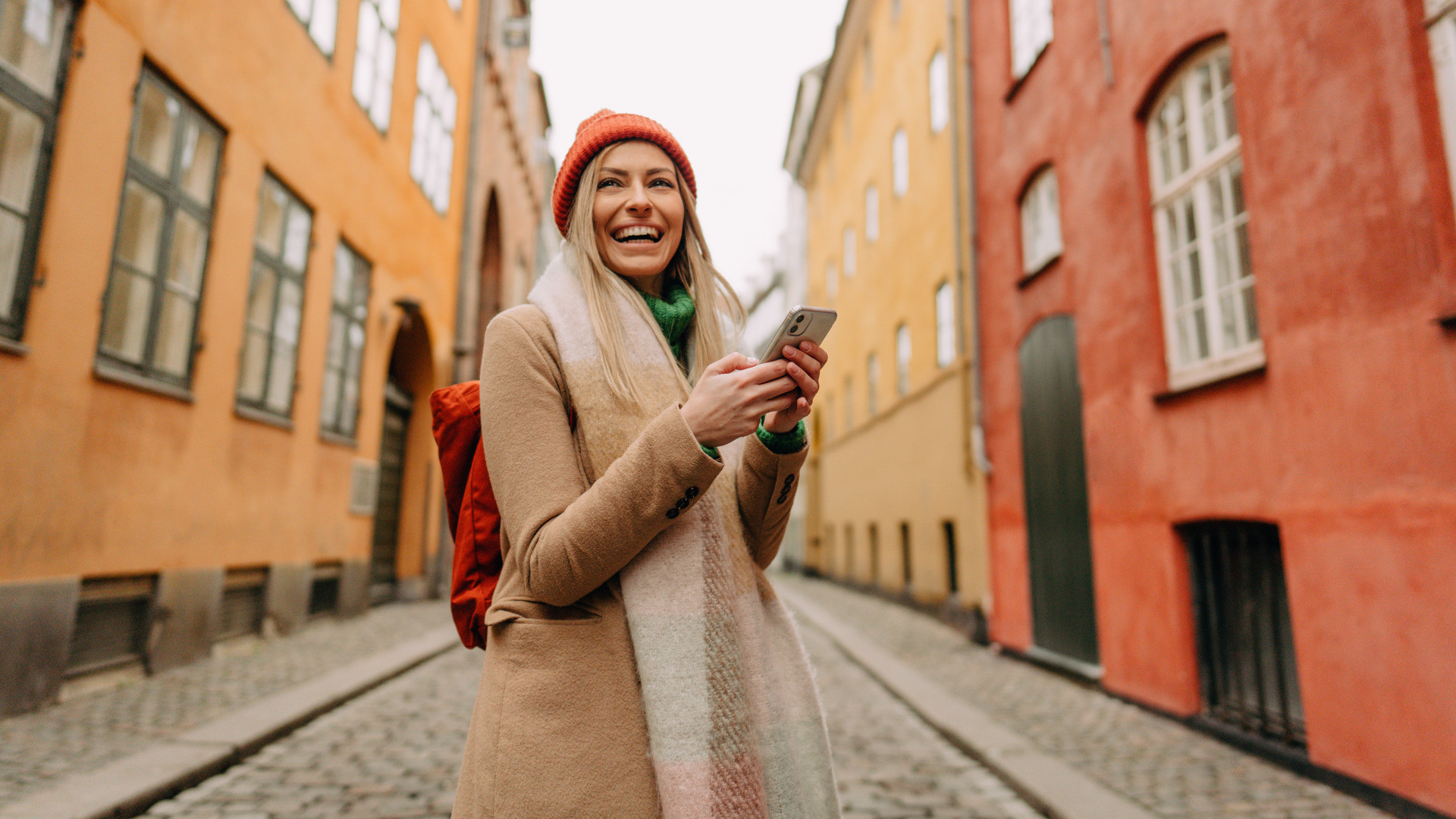Kvinne med lue står i en gate med gammel bebyggelse