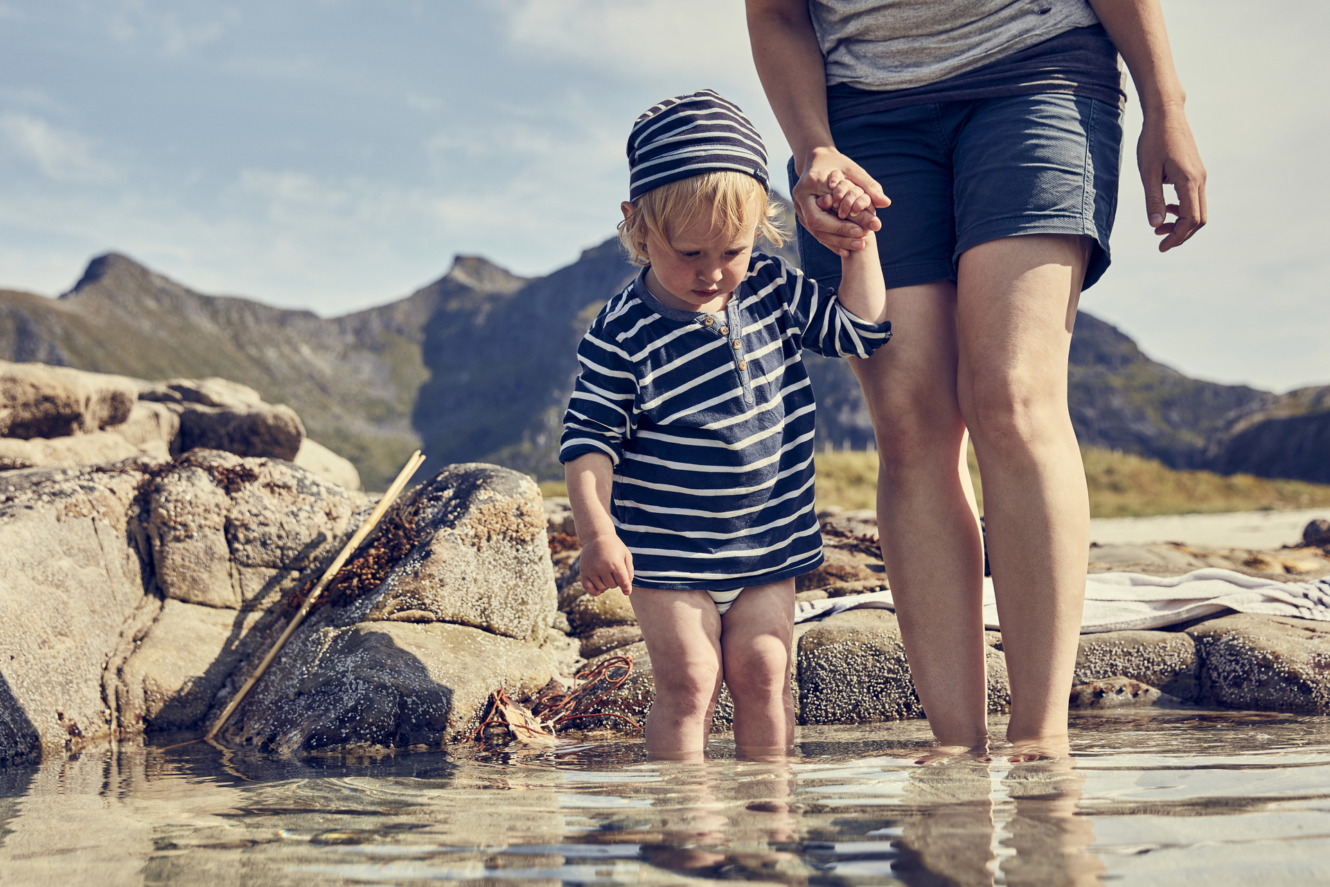 Et barn på 2-3 år holder bestemoren mens de vasser i vannet en norsk sommerdag
