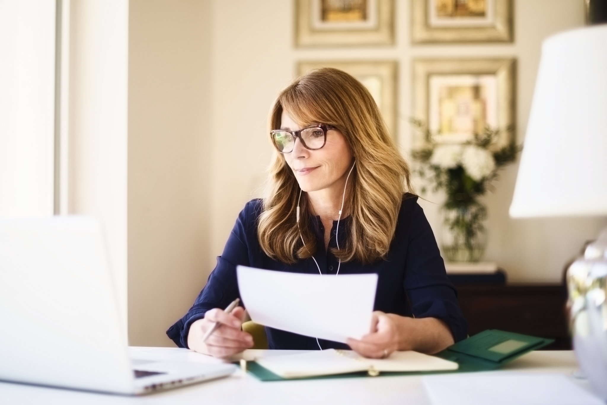 Kvinne med langt hår og briller sitter foran PC'en og sorterer papirer